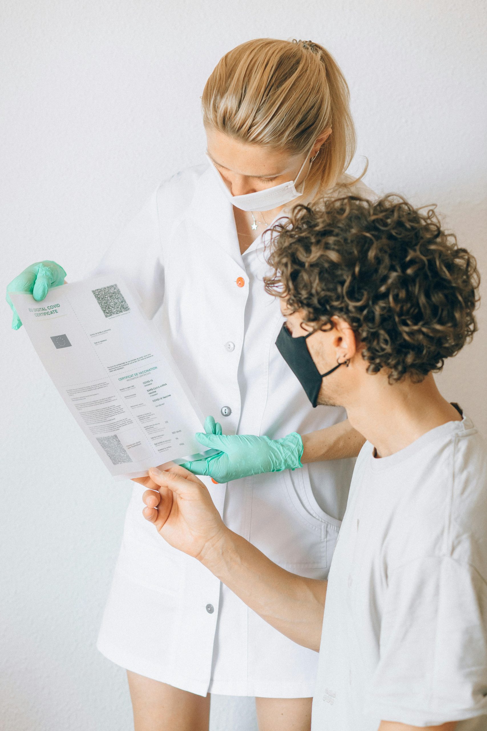 A healthcare worker and patient discussing a COVID-19 document indoors, with masks on for safety.