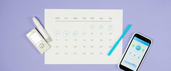 Flat lay of calendar with medical devices and smartphone, representing diabetes management.